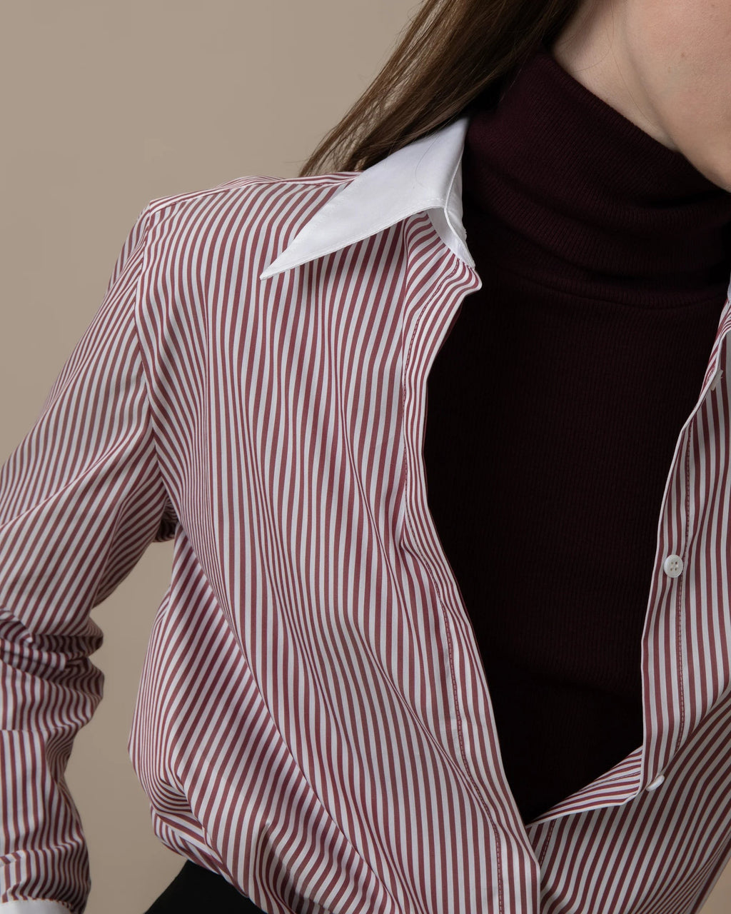Maison Sarava women's fitted burgundy and white striped shirt with a white pointed collar, worn over a dark turtleneck.