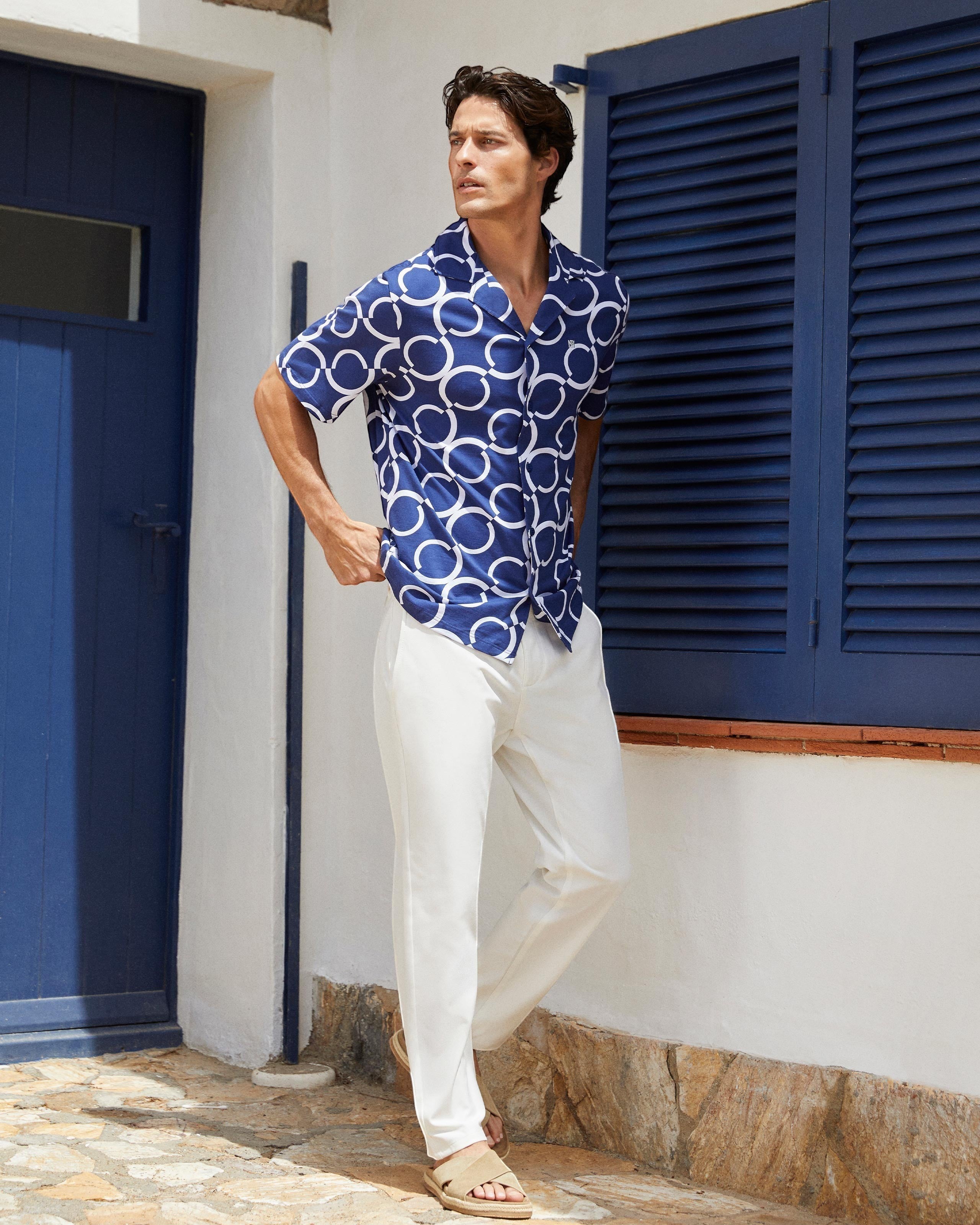 Maison Sarava navy and white geometric print short sleeve resort shirt worn by a man with white pants.
