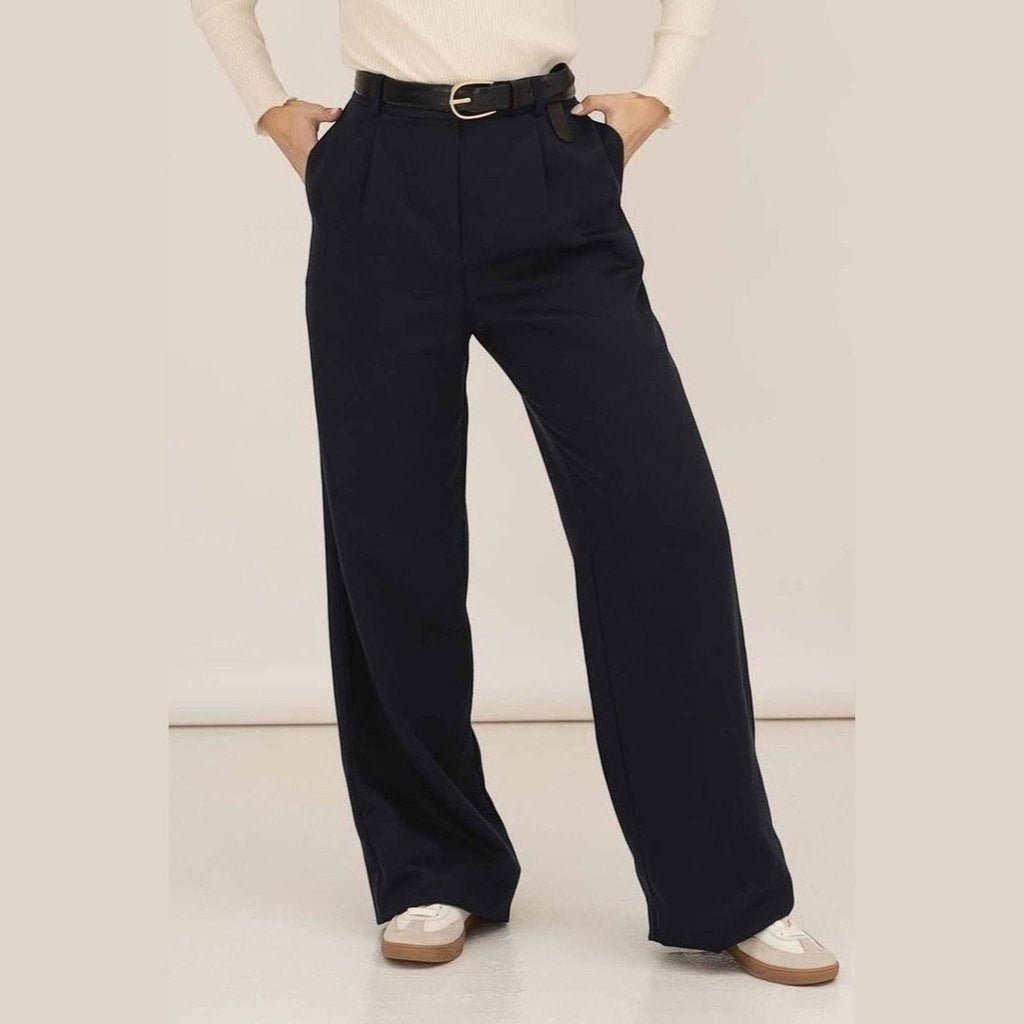 Maison Sarava navy wide leg pleated trousers with a black belt and white top, styled with sneakers.