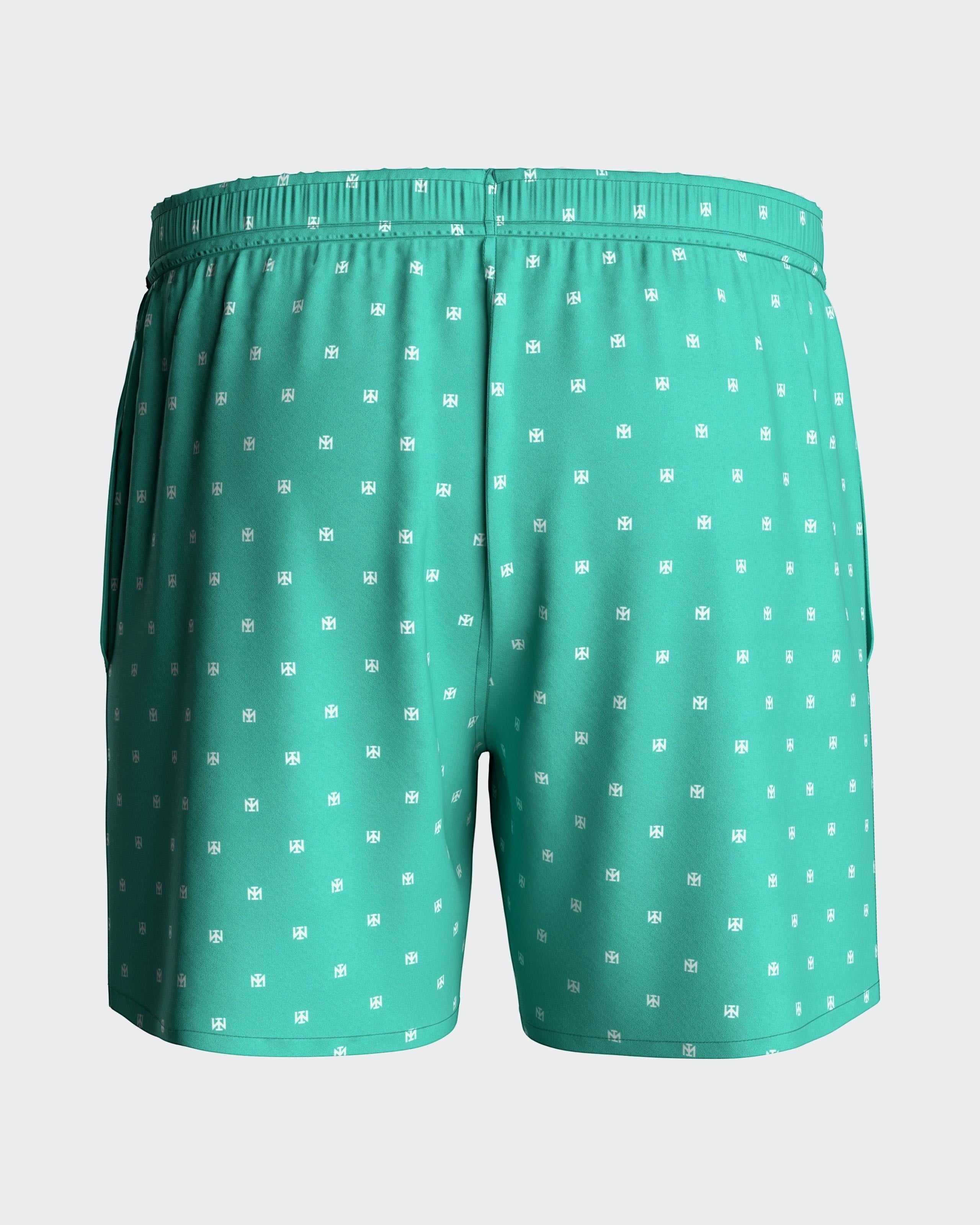 Maison Sarava men's teal swim trunks with white micro-pattern logo, elastic waistband, drawstring, and side pockets.