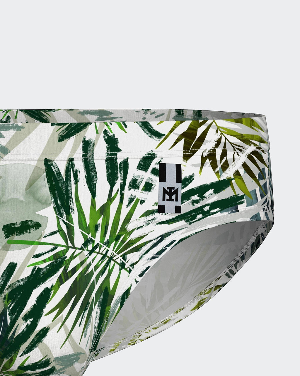 Maison Sarava white swim briefs with a bold green tropical leaf print and a black logo tag.