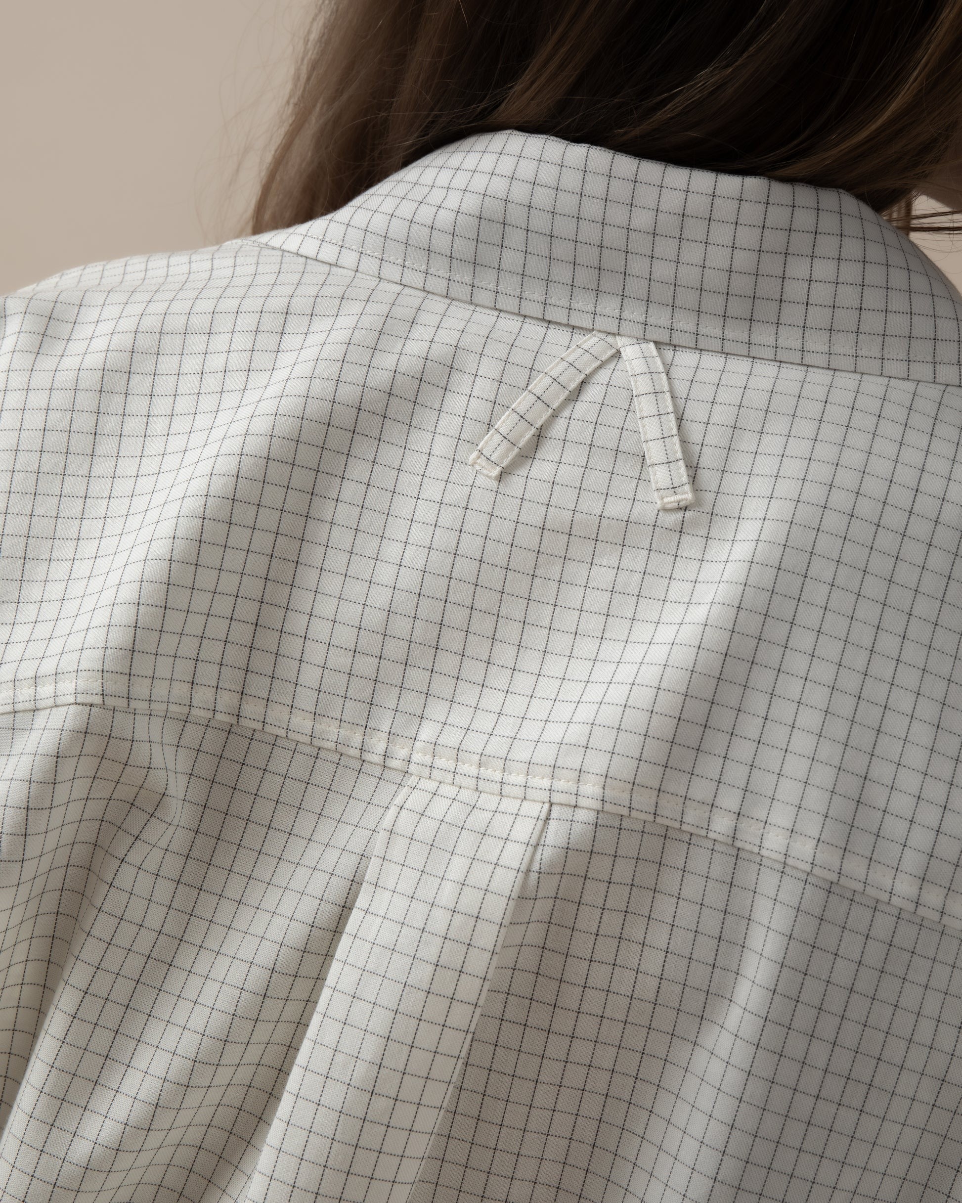 Maison Sarava women's white oversized shirt with black grid pattern, pointed collar, and unique A-design back loop detail.