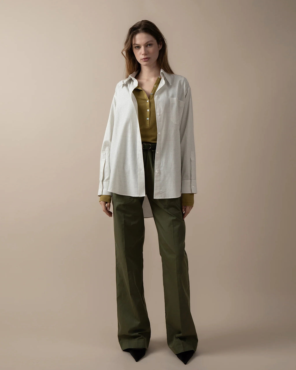 Maison Sarava women's oversized white and grey checkered shirt with pointed collar, long sleeves, and round hem, worn over a green top.