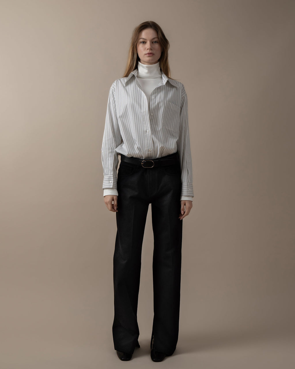 Maison Sarava women's oversized white and black pinstripe shirt with pointed collar and button cuffs, worn over a white turtleneck.
